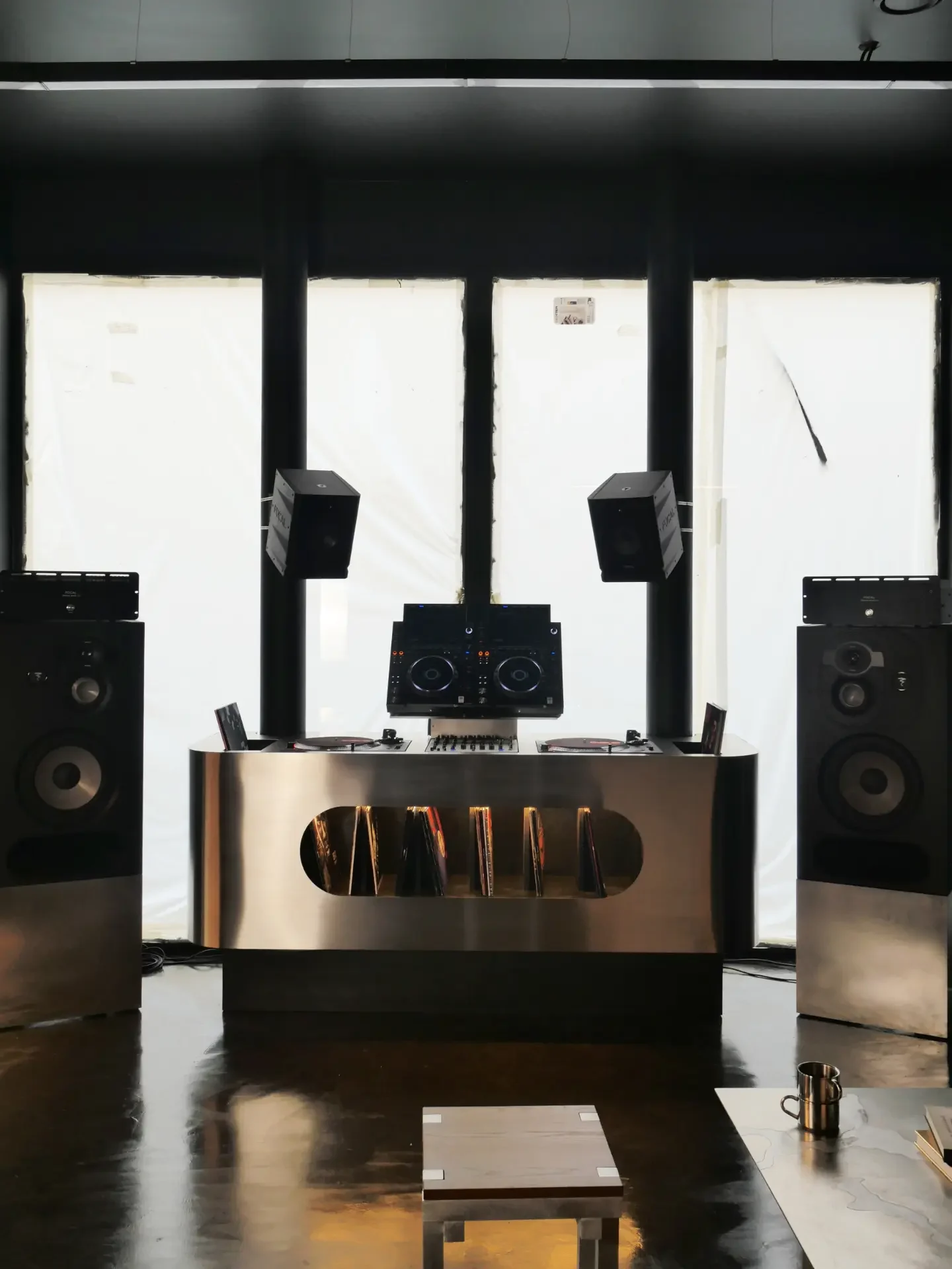 Cabine DJ en inox de face, entre deux grandes enceintes Focal, avec deux enceintes suspendues au-dessus